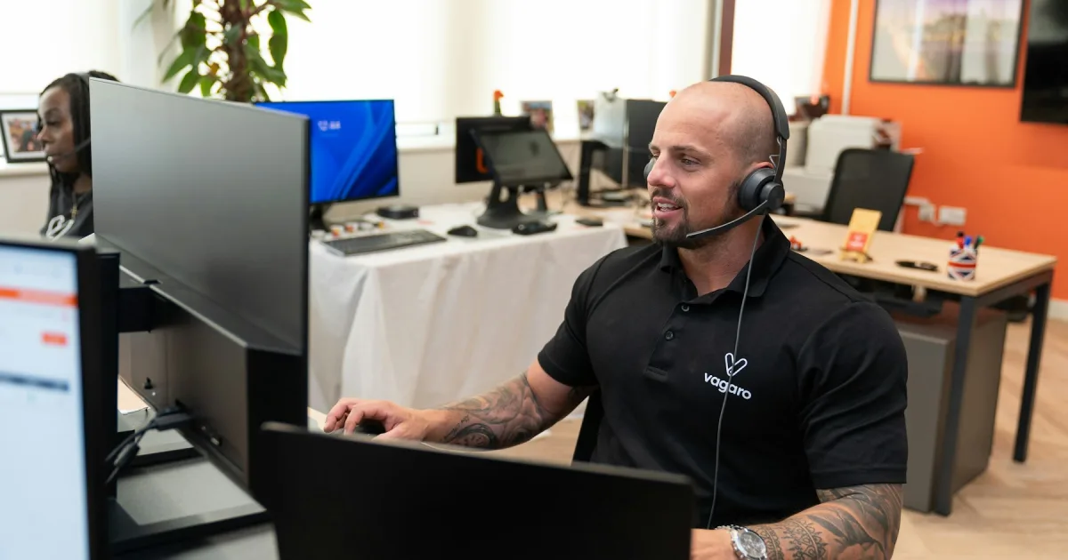 A support agent at a desk with a headset, helping a customer on screen