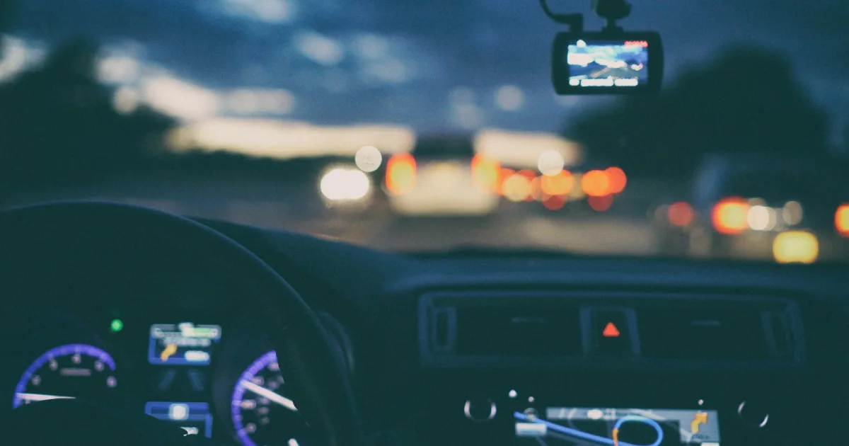 A car dashboard and steering wheel, with traffic ahead through the windscreen