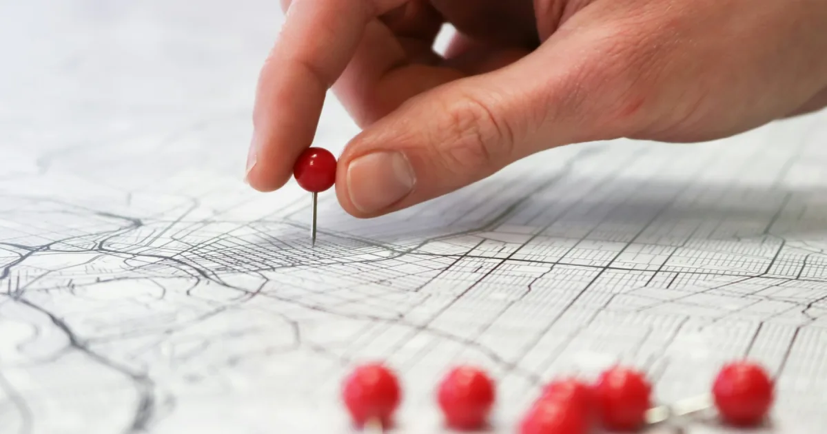 Red push pins being placed into a printed city street map