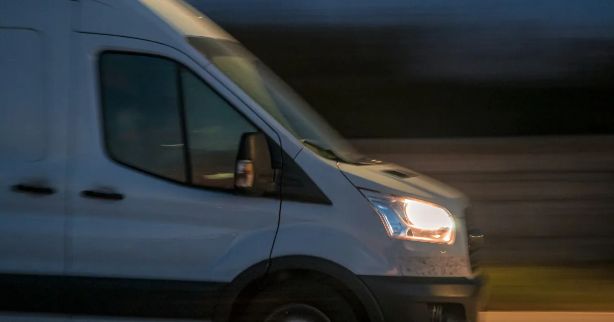 A white van driving down a street after dark