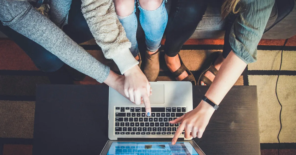 Several pairs of hands gathered around one laptop