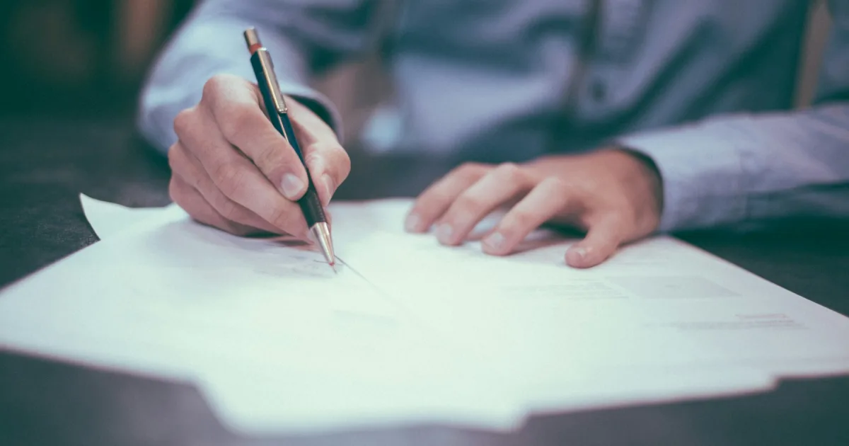 A hand writing on a blank sheet of paper at a desk