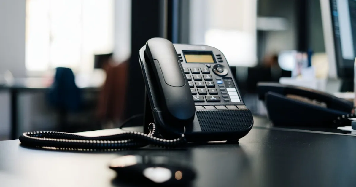 A desk phone on an office desk, with the handset resting on its cradle