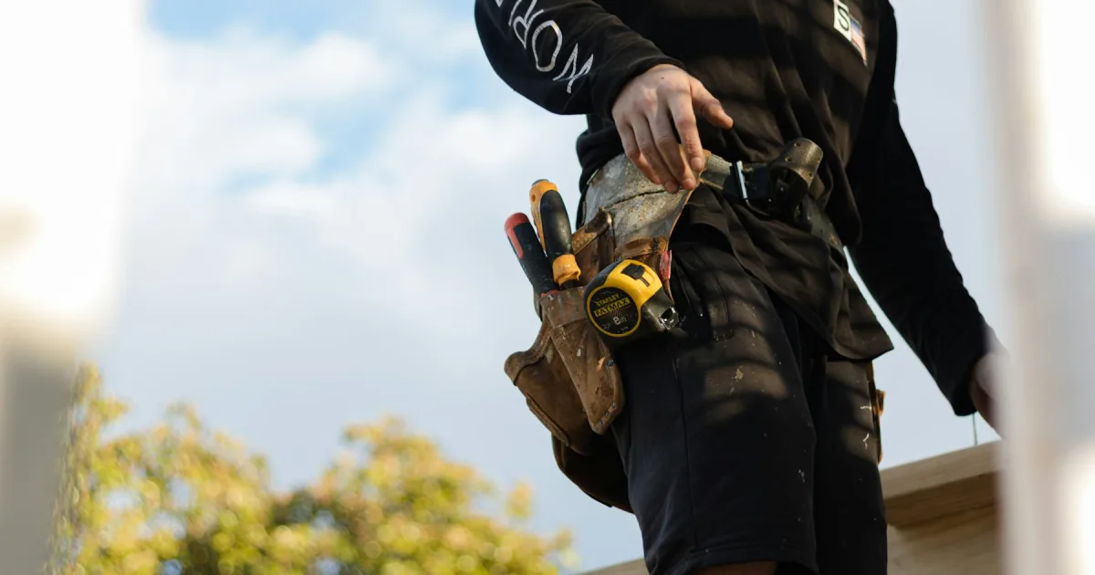A worker wearing a loaded tool belt, seen from behind against the sky