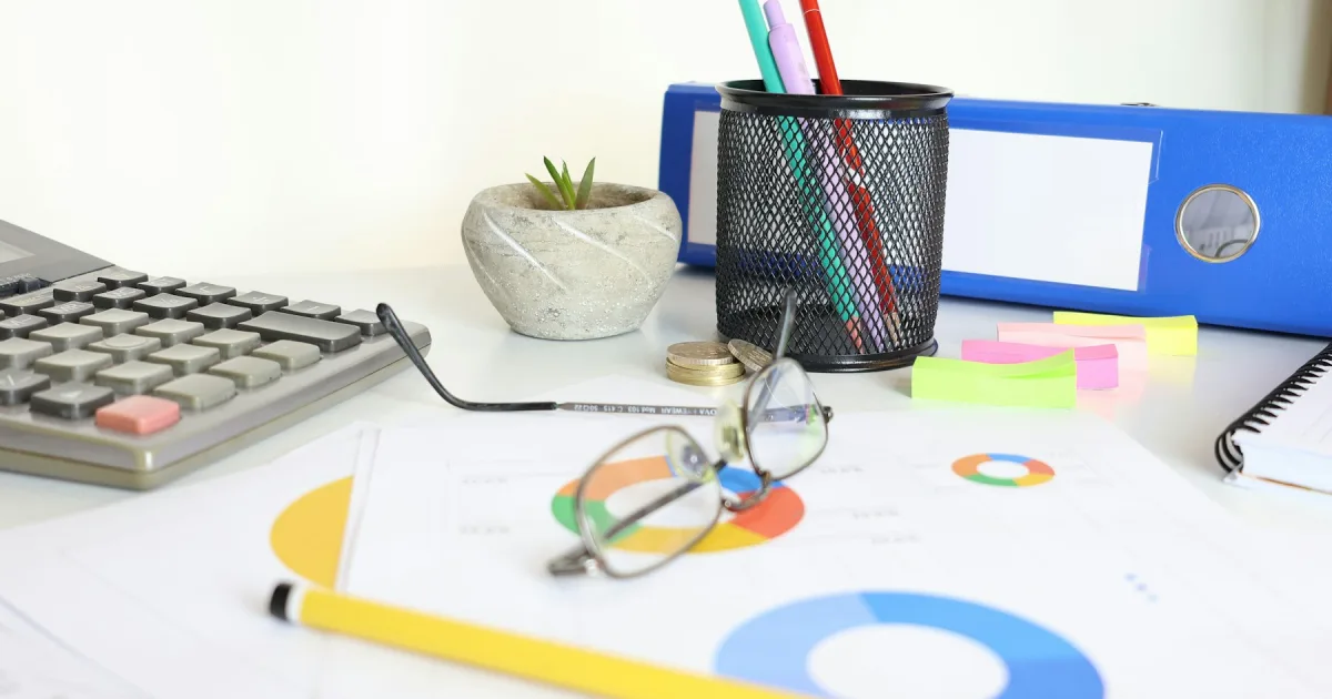 A desk with a calculator, printed charts and reading glasses