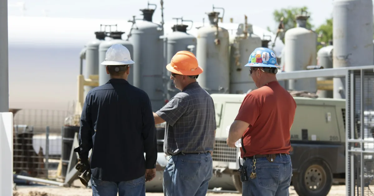 Three workers in hard hats discussing equipment on site
