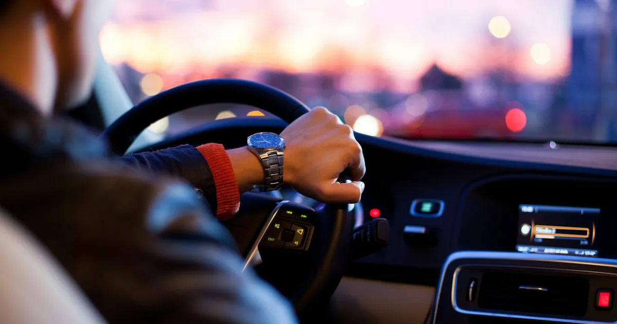 A hand on a steering wheel at night, with city lights blurred ahead